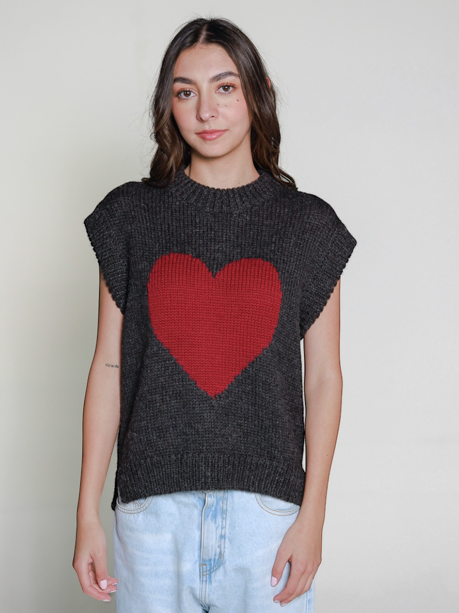 Person wearing a dark gray sleeveless sweater vest with a burgundy heart design on a plain background