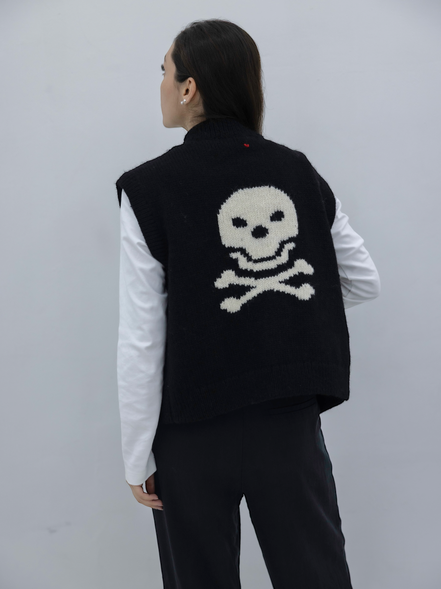 women wearing a knitted alpaca vest in black with skull and crossbones design a white background