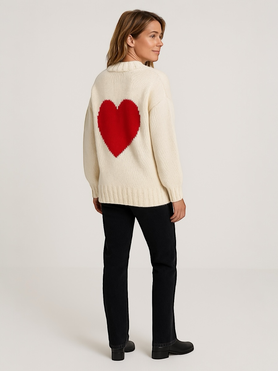 Woman wearing a cream sweater with a red heart design on a plain background
