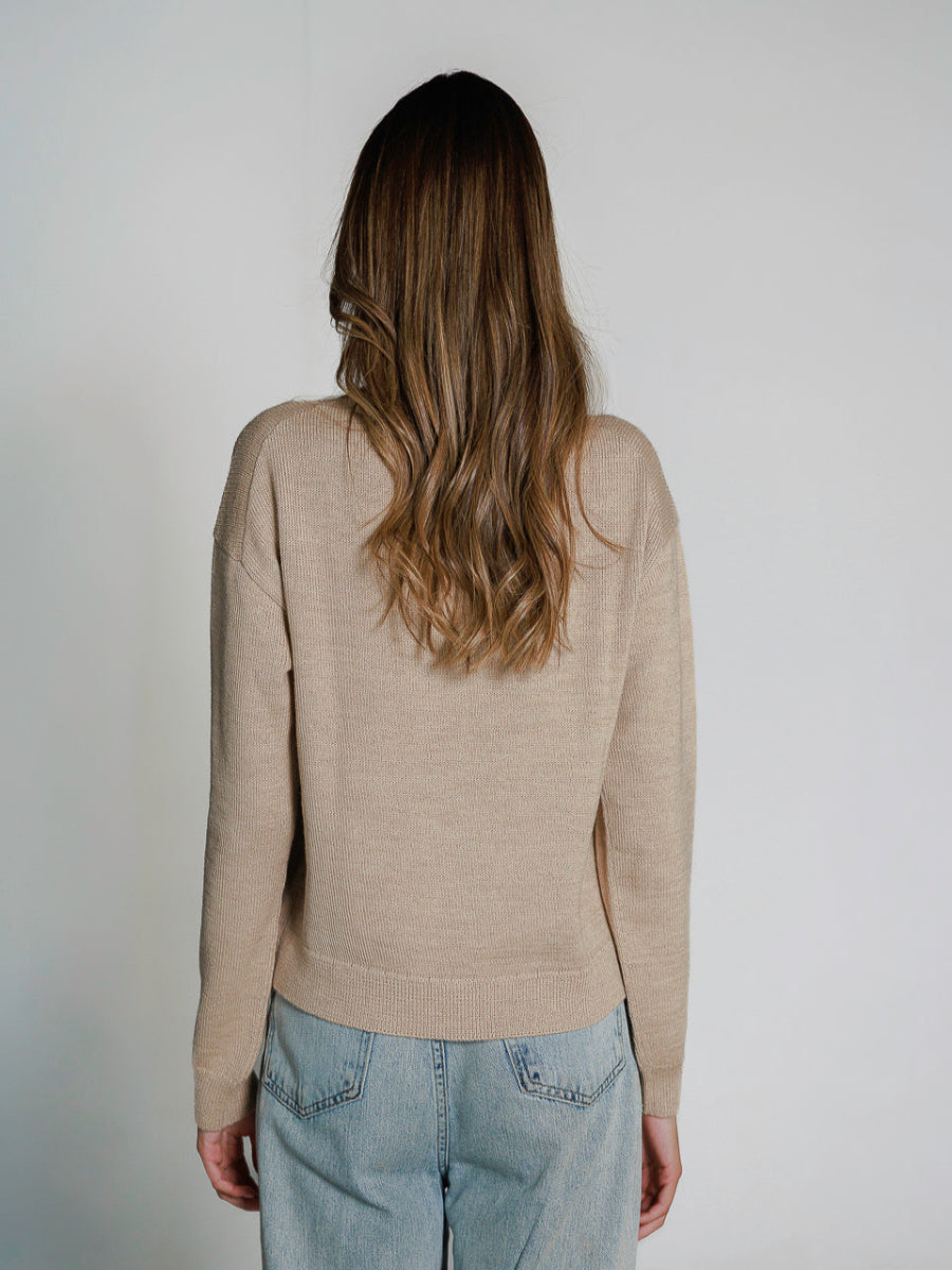 Beige alpaca knitted sweater featuring a playful alpaca face design on the front, worn by a model backwards on a white background.