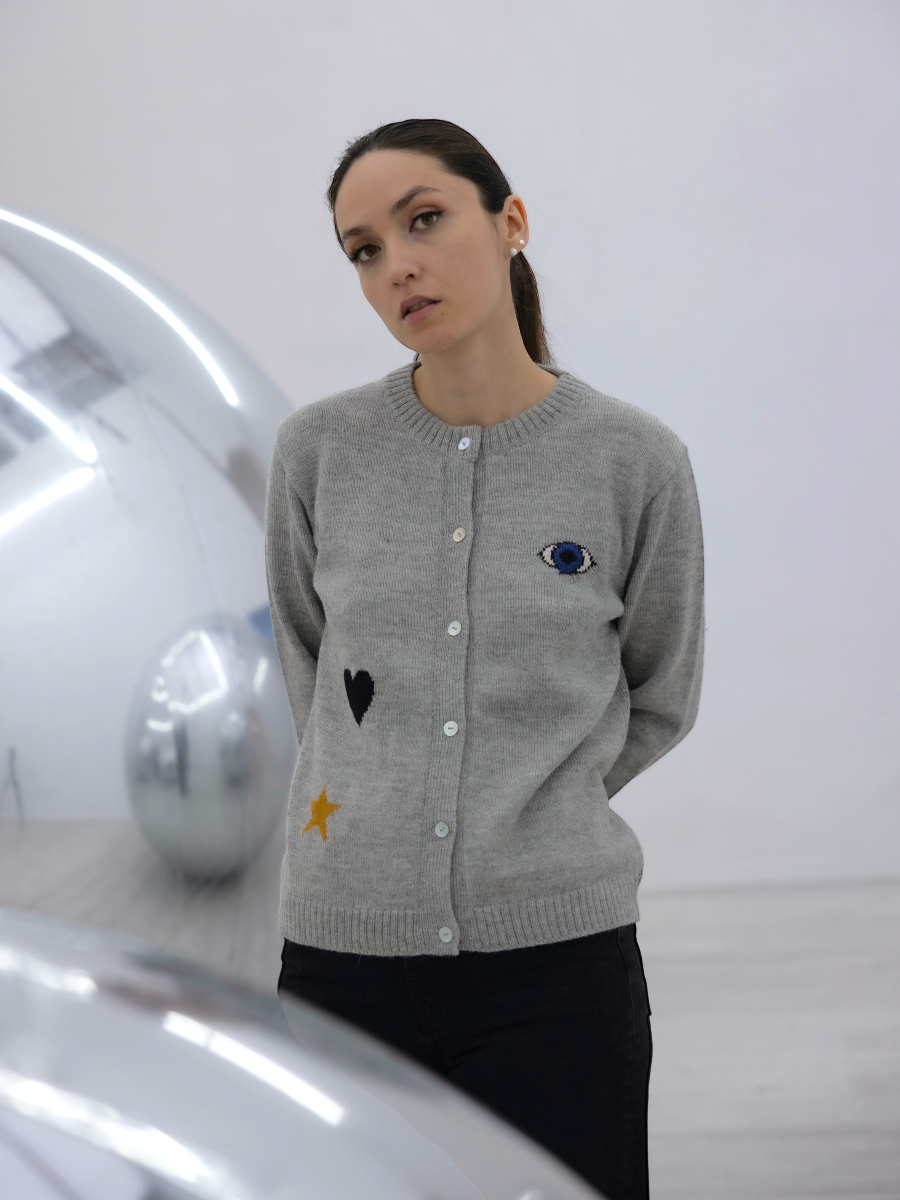 Woman wearing a gray cardigan with embroidered designs in a minimalistic setting