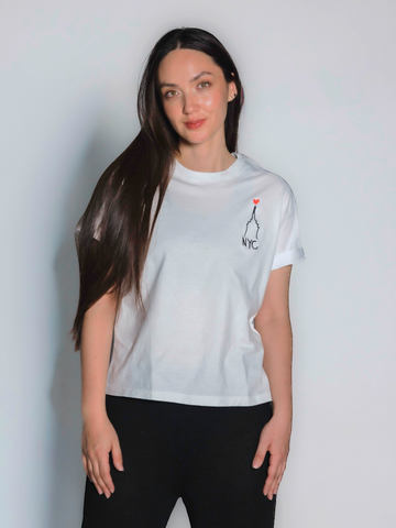 White cotton t-shirt featuring a minimalist embroidered New York City skyline with a small red heart and “NYC” lettering on the front, shown here on a model with a plain background