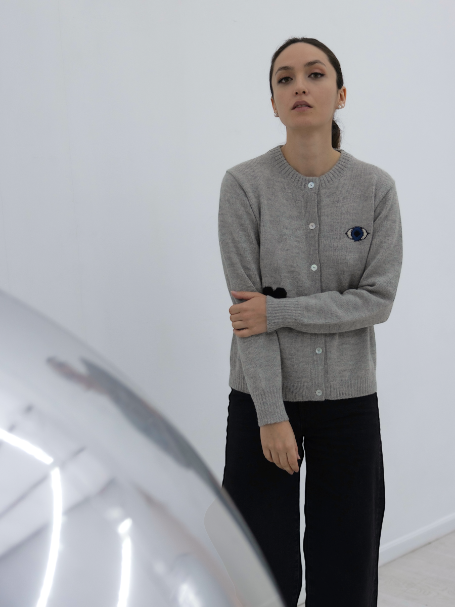 grey button up cardigan decorated with a Turkish eye, black heart and a yellow star, worn by a model on an art gallery