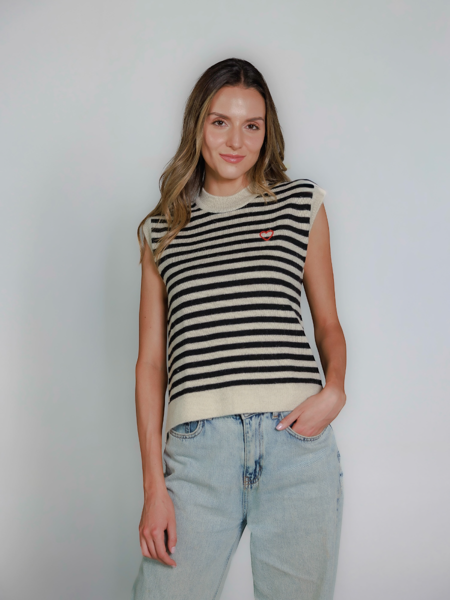 Woman wearing a striped sleeveless knitted vest and jeans on a plain background