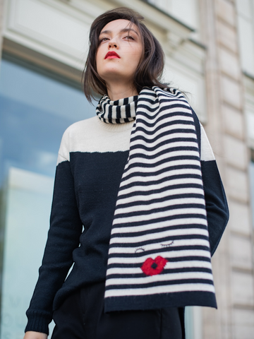 Black-and-white striped alpaca scarf featuring an embroidered face motif with closed eyes and red lips styled with a yapa sweater, shown on a model against an outdoor background.