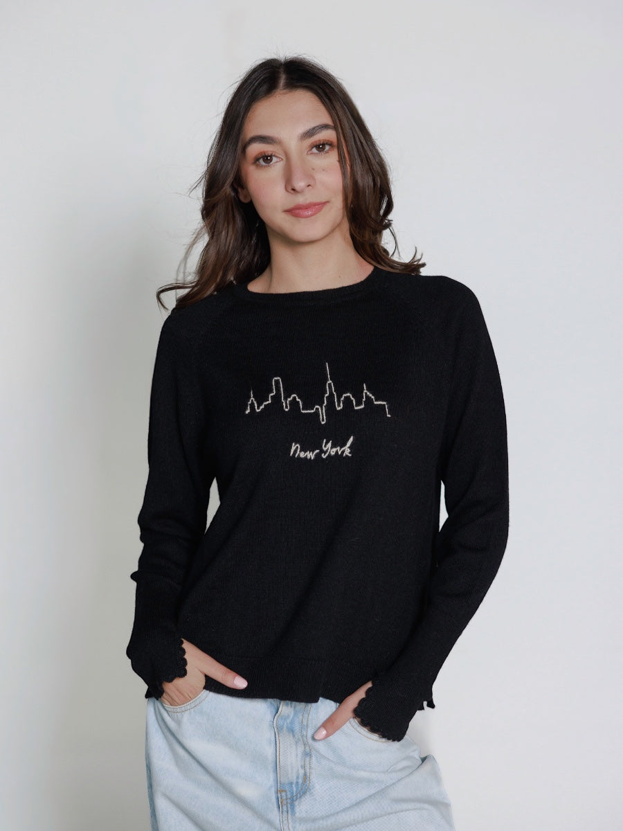 Model wearing a black hand embroidered sweater with 'New York' text and skyline on a plain background
