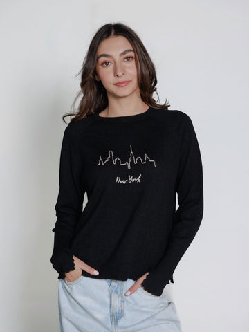 Model wearing a black hand embroidered sweater with 'New York' text and skyline on a plain background