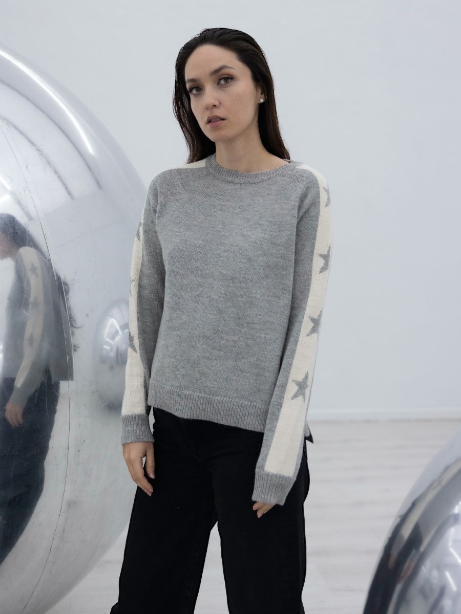 grey alpaca sweater with stars on the sleeves on model with an art gallery background