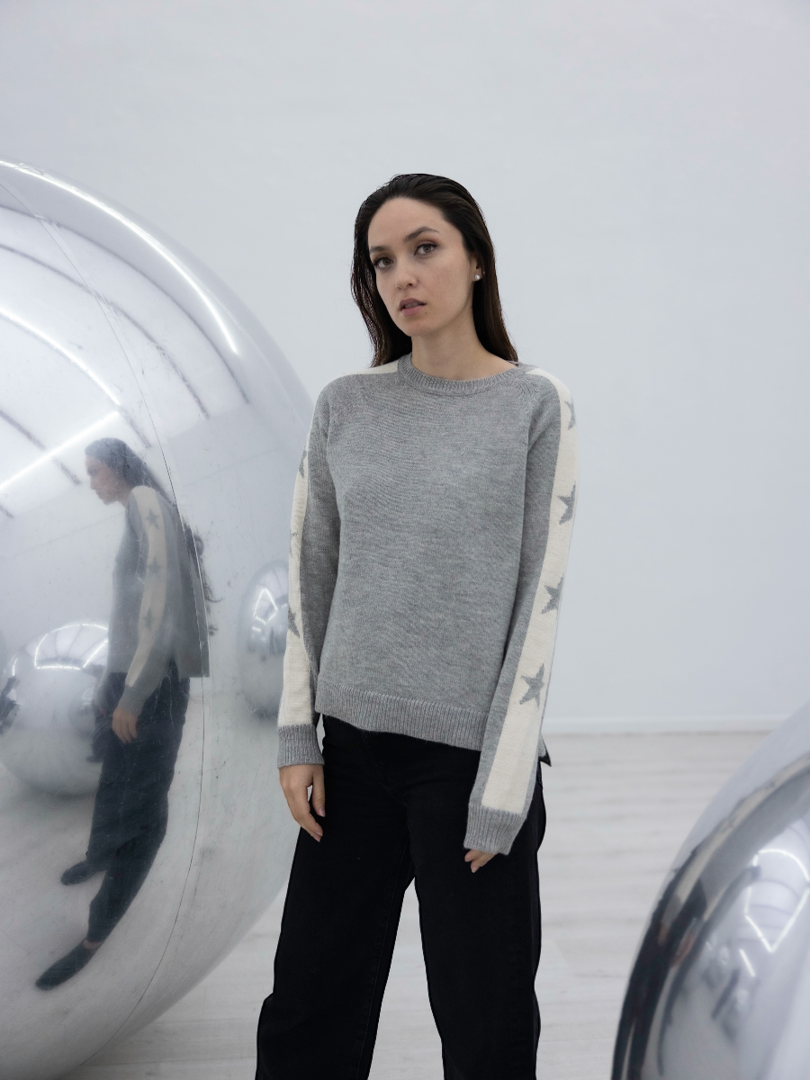 grey alpaca sweater with stars on the sleeves on model with an art gallery background