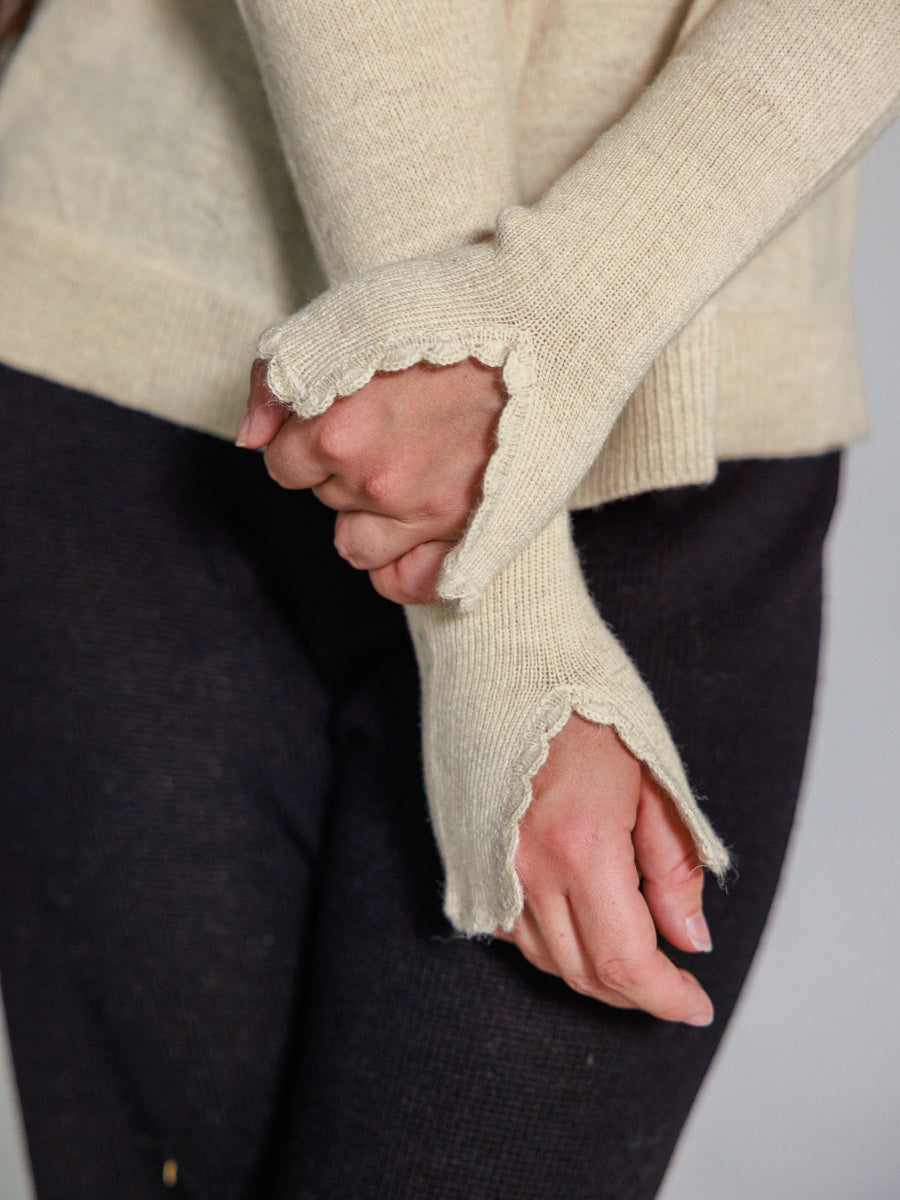 Close-up of a person wearing a beige sweater with lace cuffs on a plain background