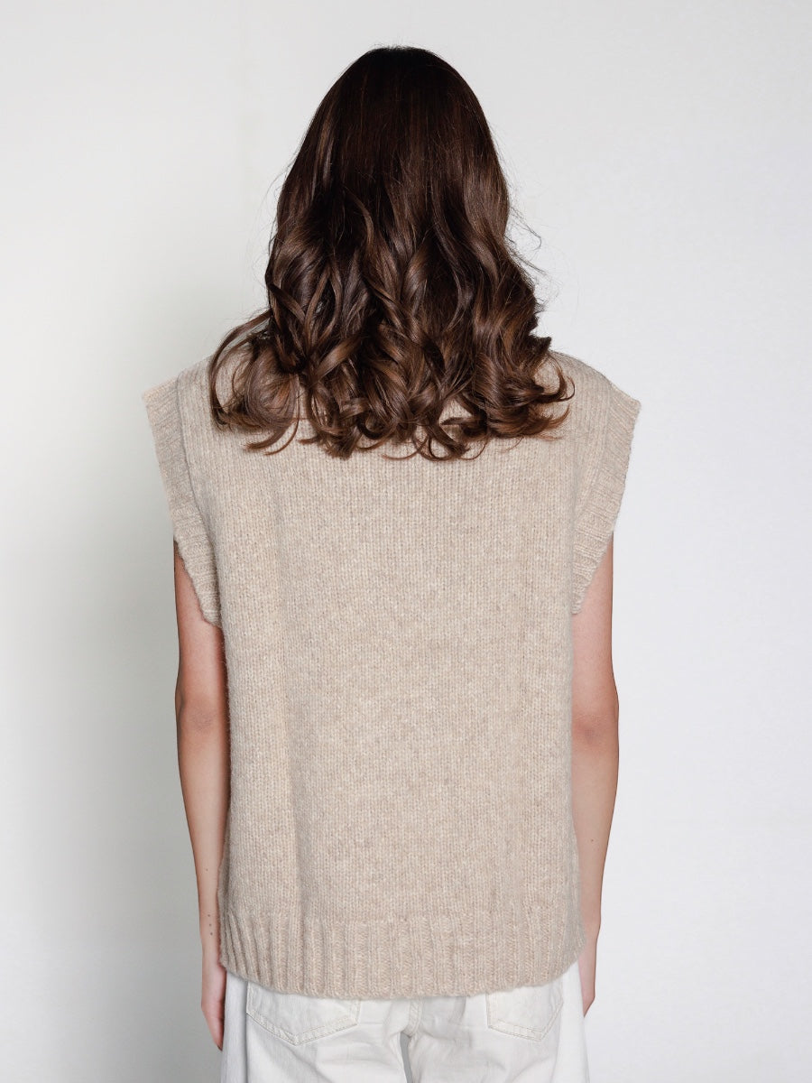 Person wearing a beige knitted vest on a white background