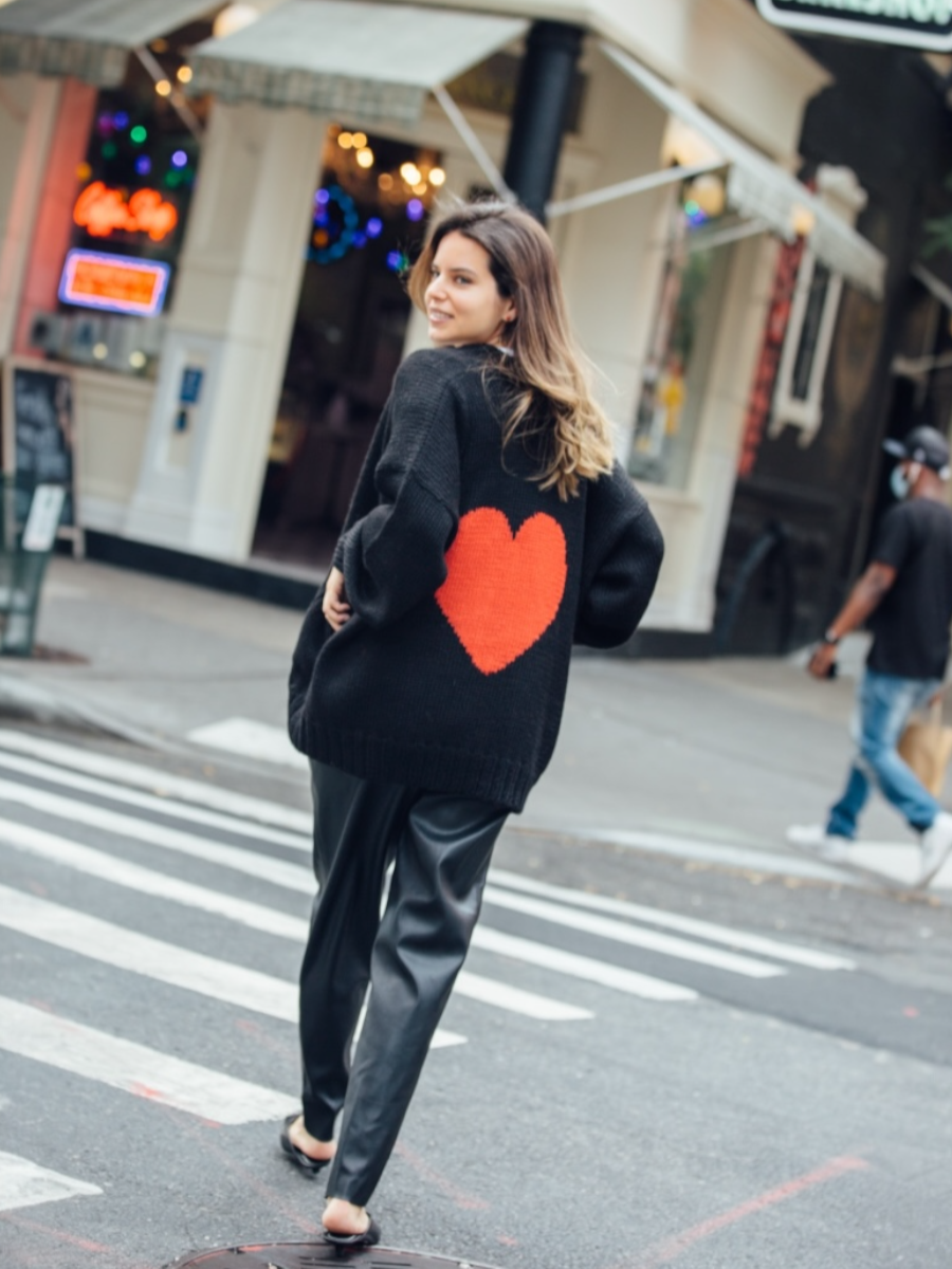 Woman wearing a black knitted cardigan with a red heart in the back walking around New York City