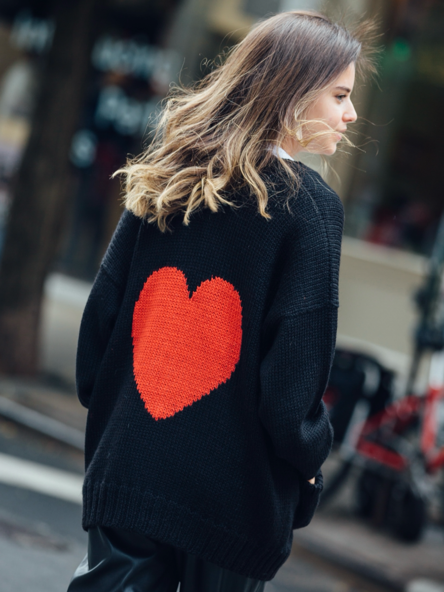 Woman wearing a black knitted cardigan with a red heart in the back walking around New York City