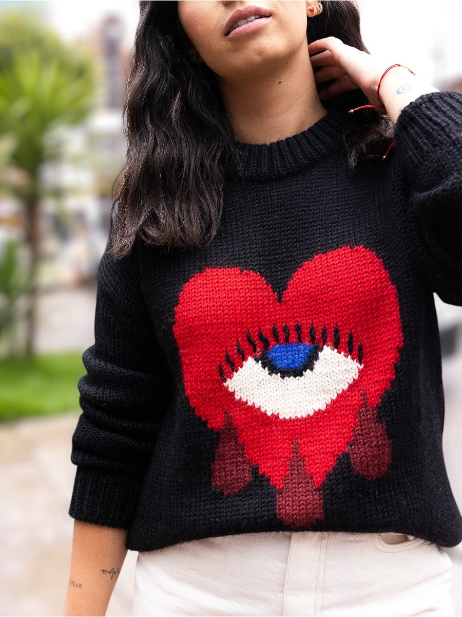 black alpaca sweater featuring a bold red heart motif with a blue eye and tear details on the front, shown here on a model.