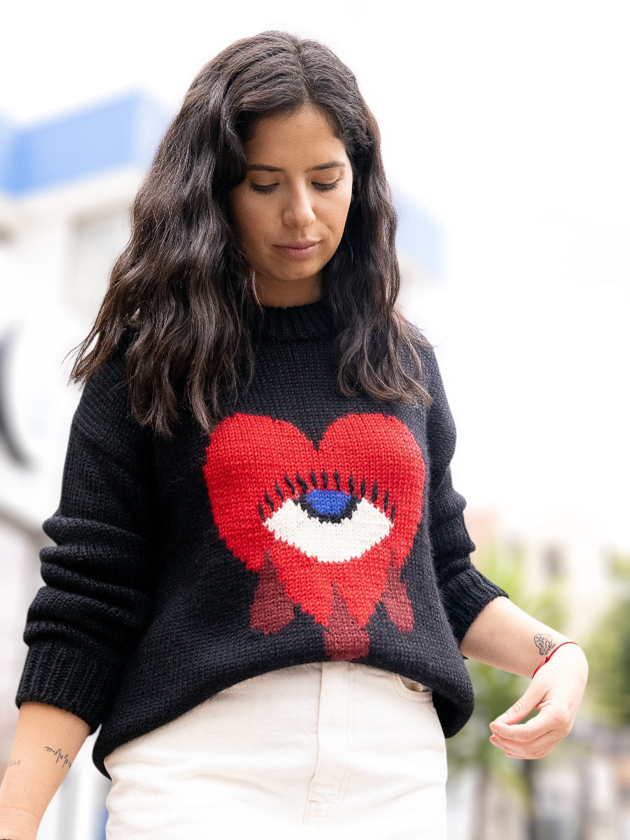 black alpaca sweater featuring a bold red heart motif with a blue eye and tear details on the front, shown here on a model.