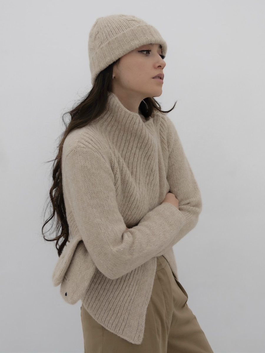 chunky beige llama knitted cardigan with unique crossed design, worn by a model styled with beige yapa beanie