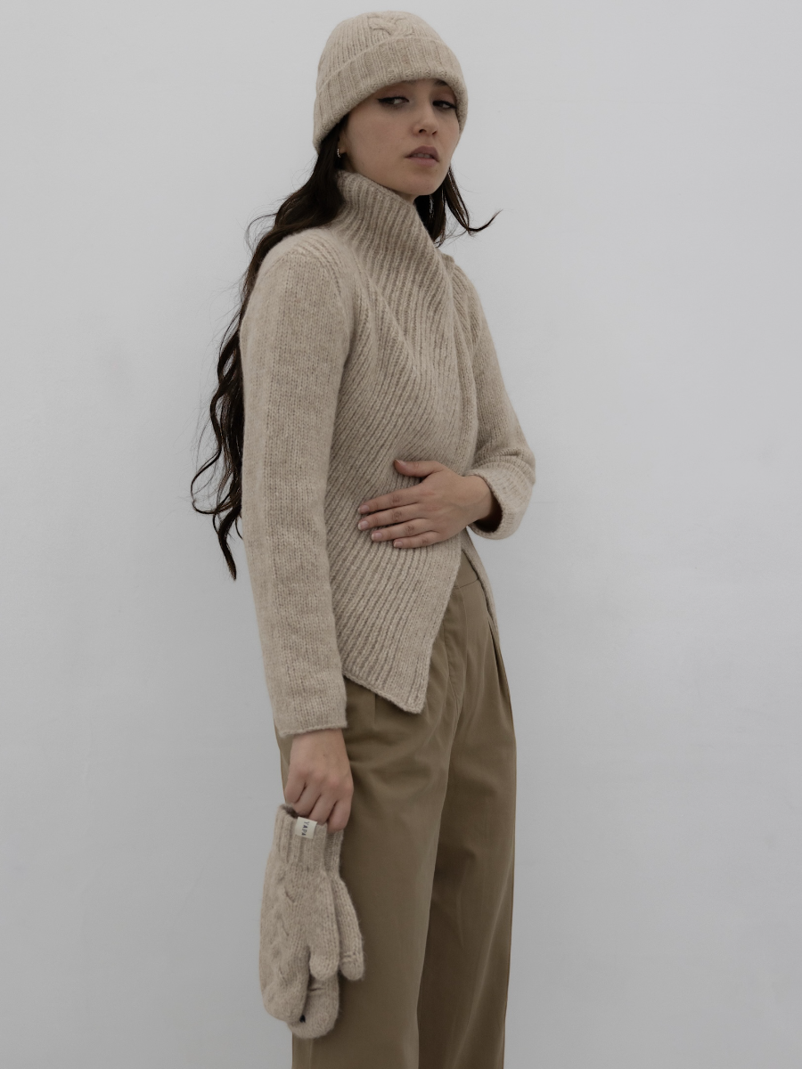 chunky beige llama knitted cardigan with unique crossed design, worn by a model styled with beige yapa beanie