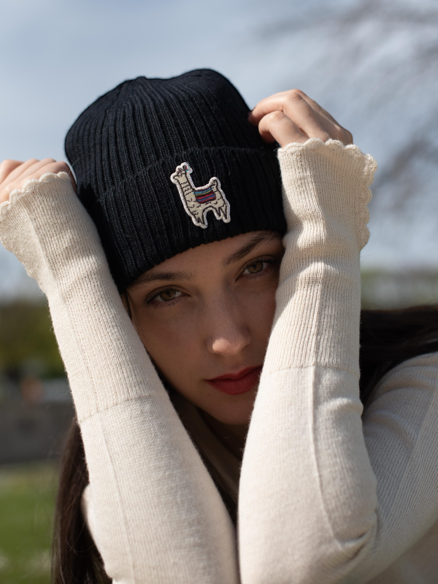 Woman wearing a black knit beanie with a llama design outdoors