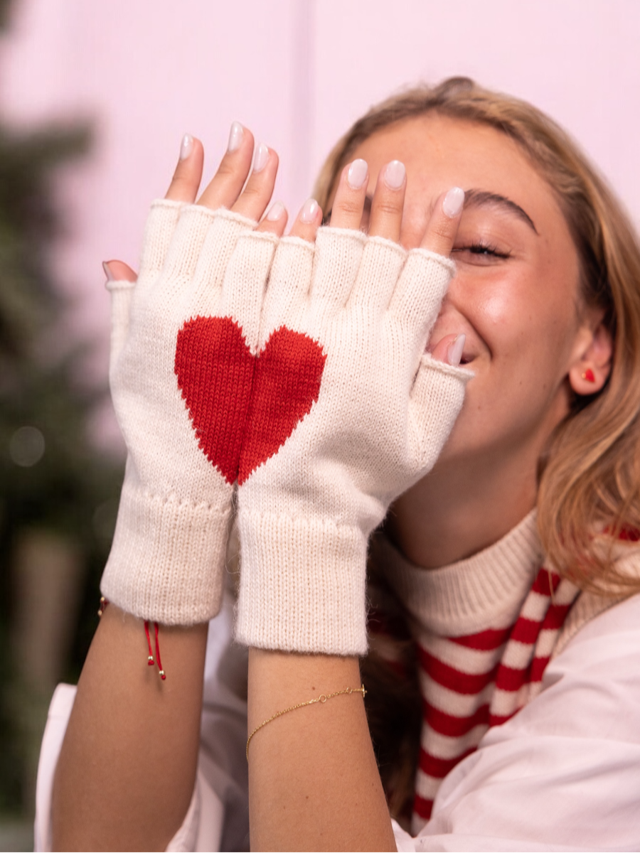 Model wearing white alpaca knitted fingerless gloves with a red heart design that forms when she join hands