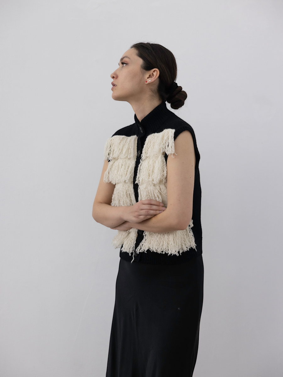 white alpaca fringed button-up vest with black rib, shown on a model against a white background