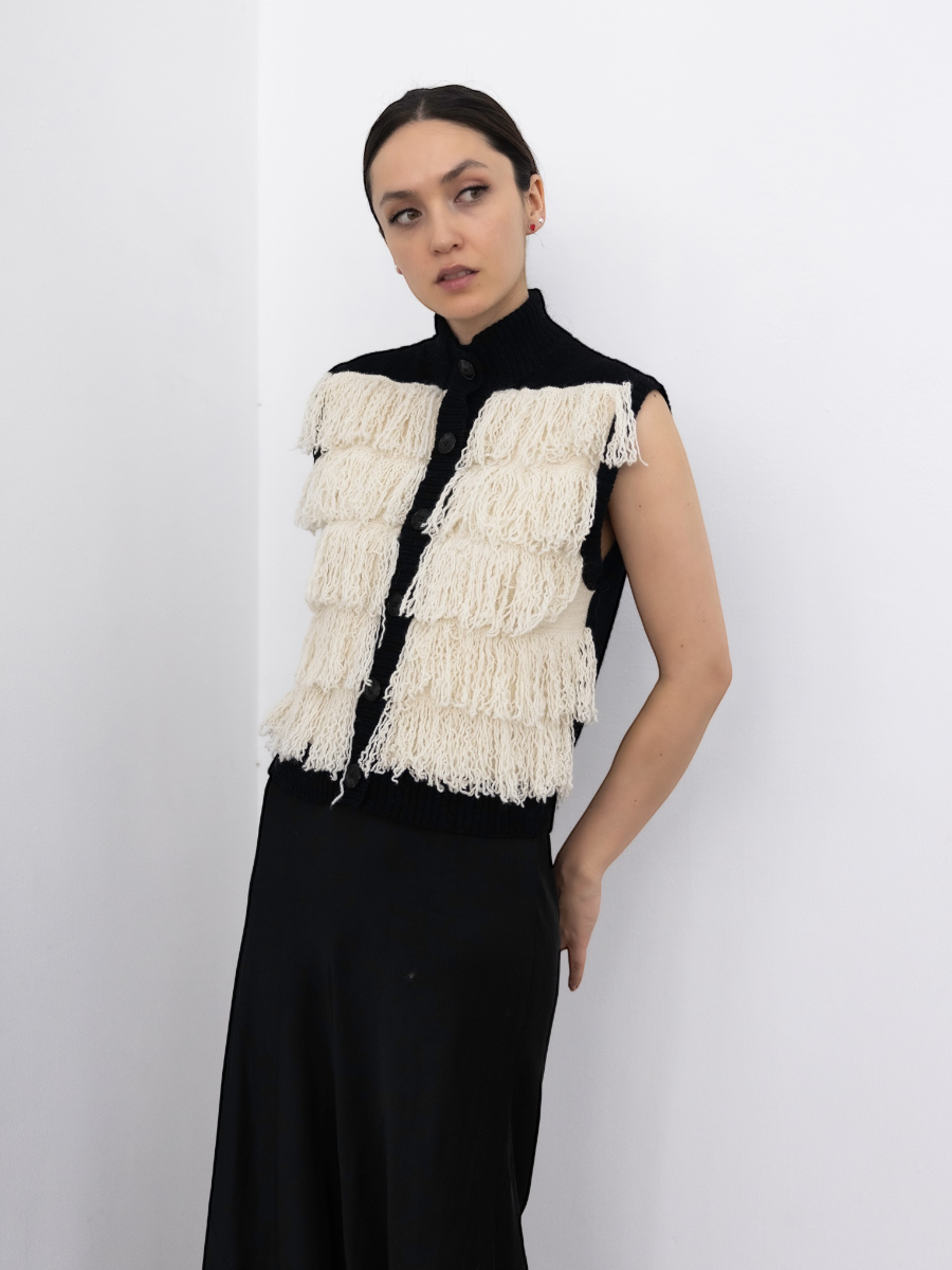 white alpaca fringed button-up vest with black rib, shown on a model against a white background