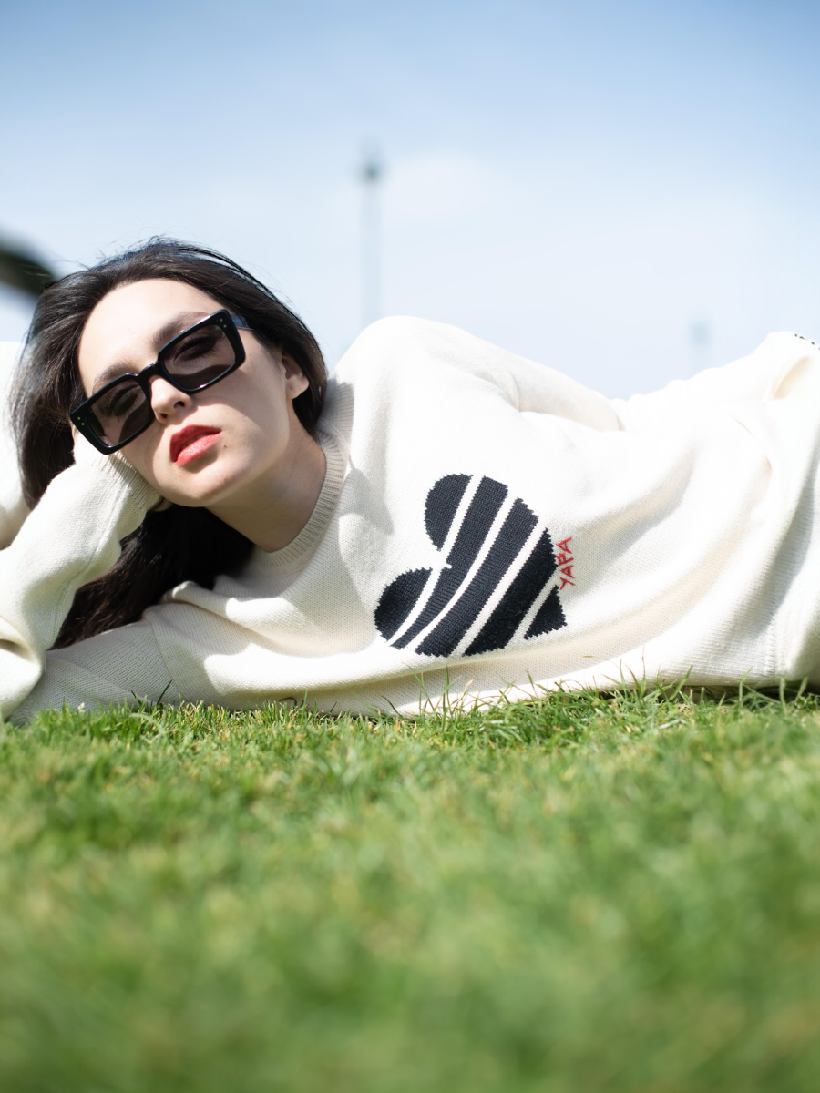 white alpaca knitted sweater with a black striped heart design, worn by a model lying on the grass