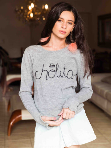 Light grey alpaca sweater featuring the word “cholita” embroidered in black script on the front, shown here on a model in an indoor setting.