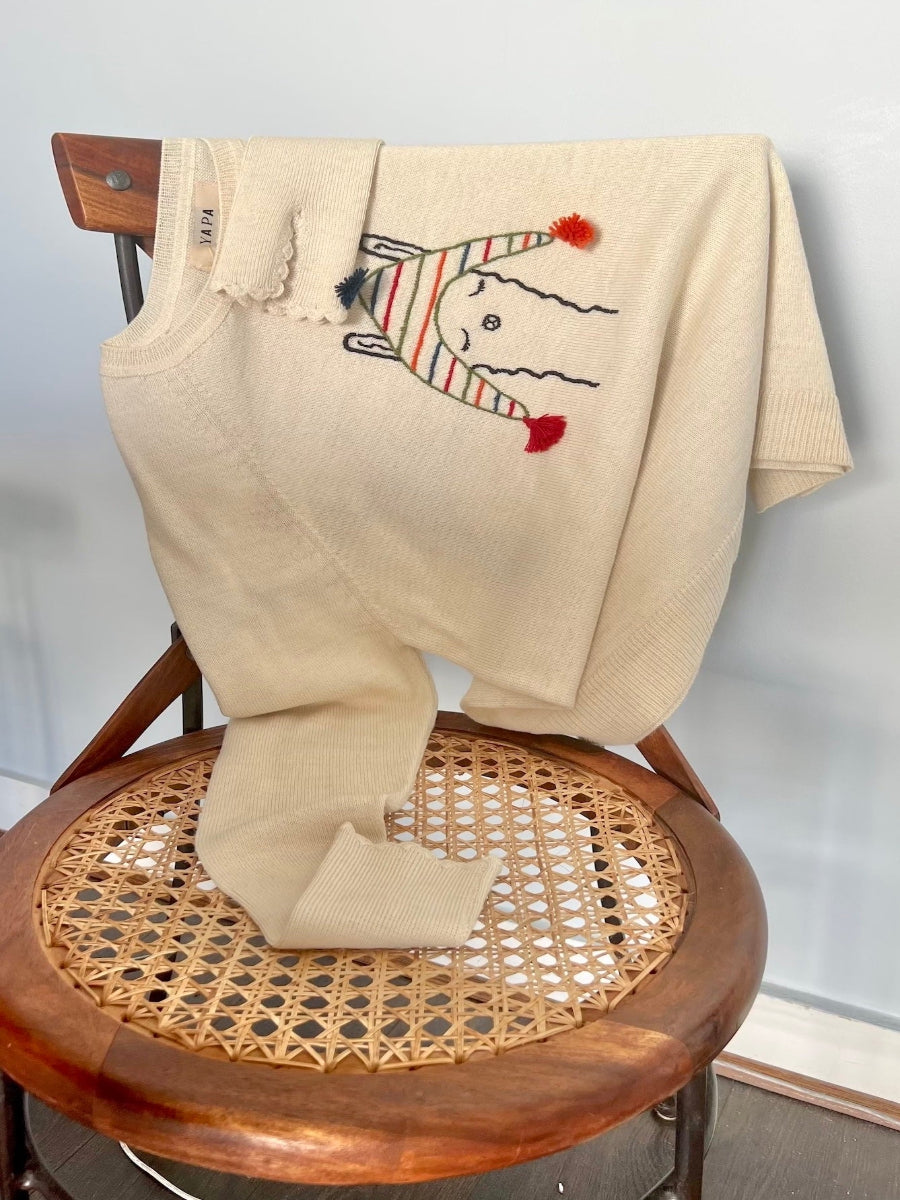 beige alpaca knitted sweater with a llama design wearing a colorful hat, folded on a chair