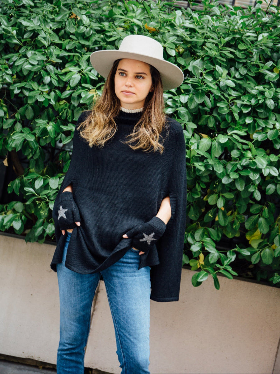 A black alpaca poncho with, worn by a model styled with star-patterned fingerless gloves and a wide-brim hat outdoors