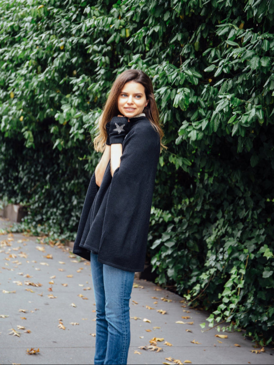 A black alpaca poncho with, worn by a model styled with star-patterned fingerless gloves outdoors