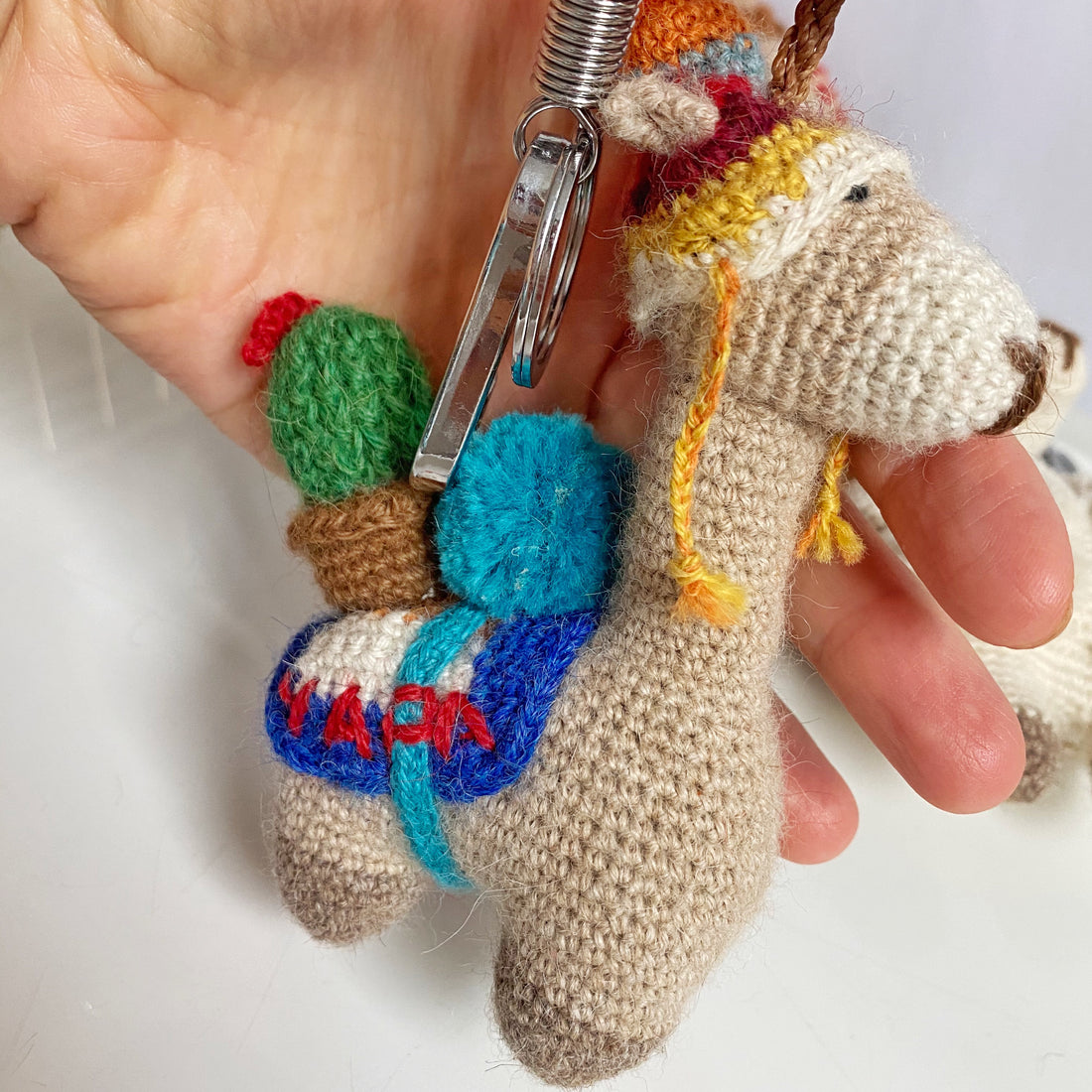 Handmade crochet alpaca keychain and bag charm with colorful details being held in a person's hand.