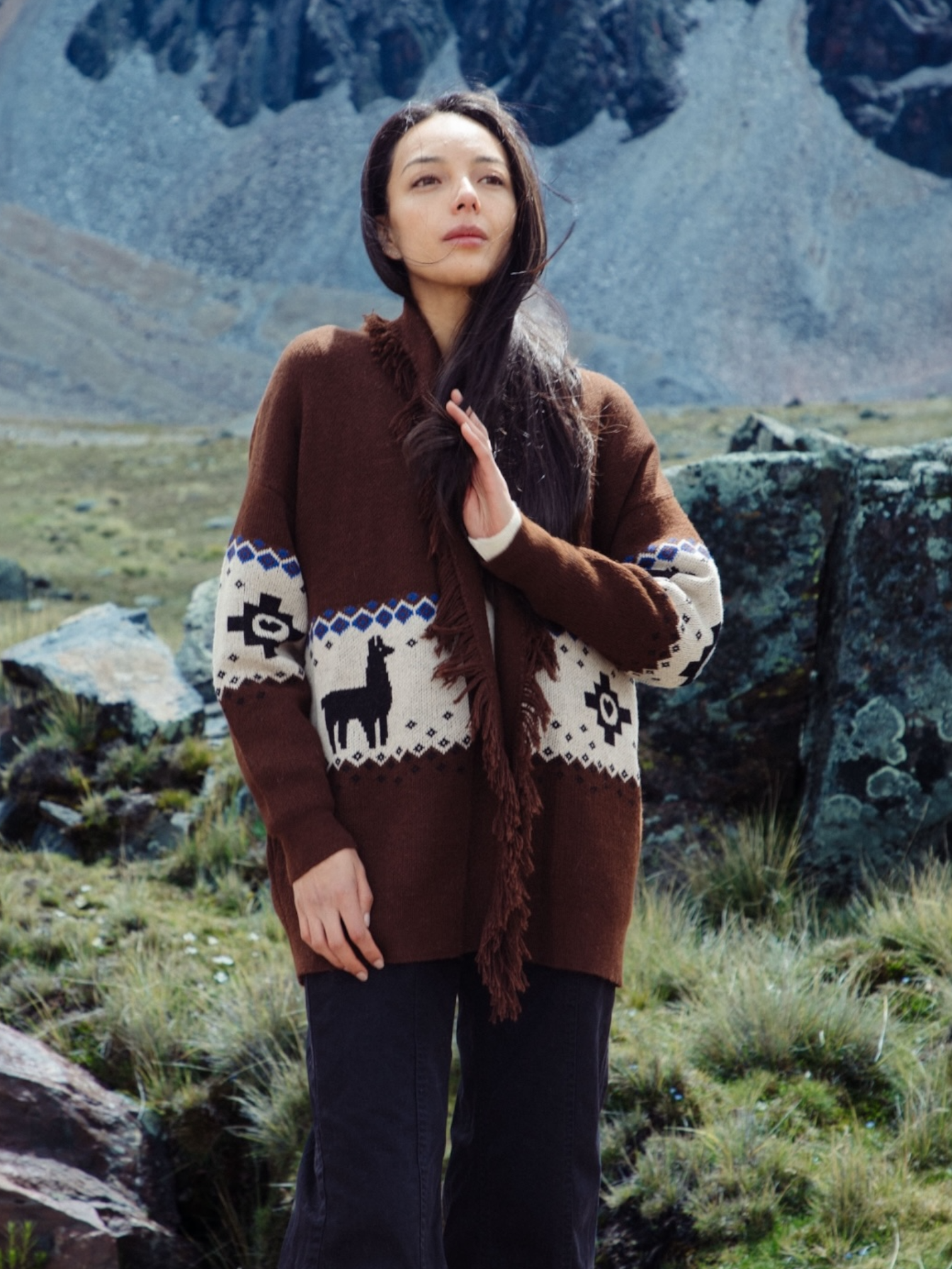Woman wearing a brown sweater with a mountainous landscape in the background