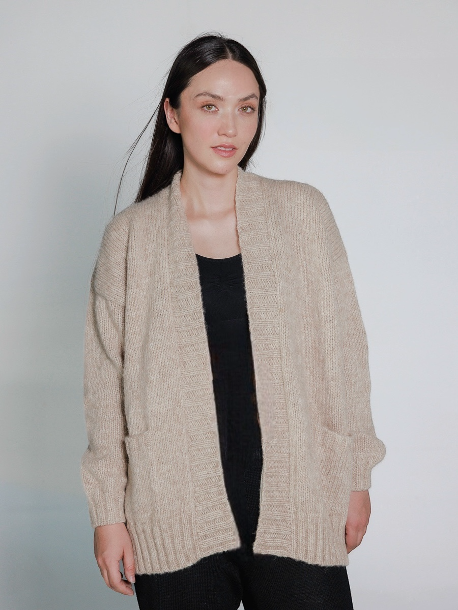 Woman wearing a beige cardigan over a black top against a plain background