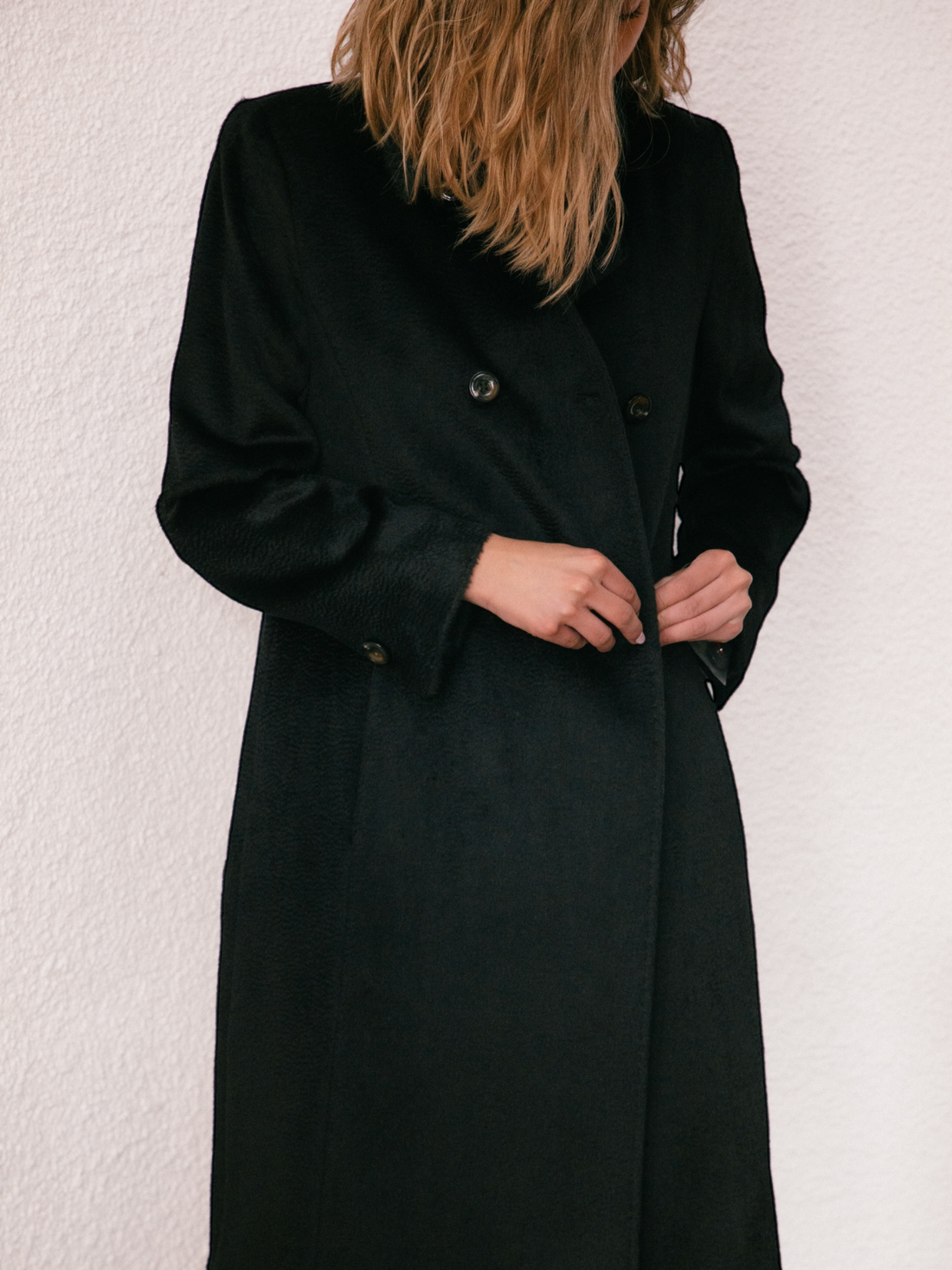 Woman wearing a black alpaca coat standing in a modern architectural setting with wooden floors and walls.