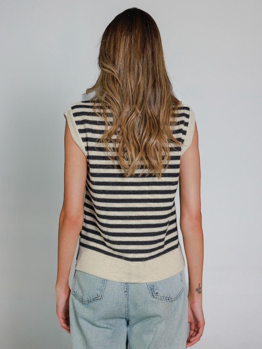 Person wearing a striped sleeveless knitted vest and jeans against a plain background