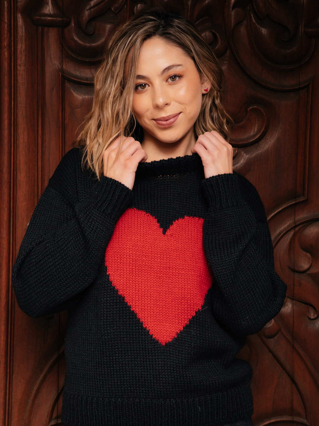 Woman wearing a black sweater with a red heart design against a decorative brown background
