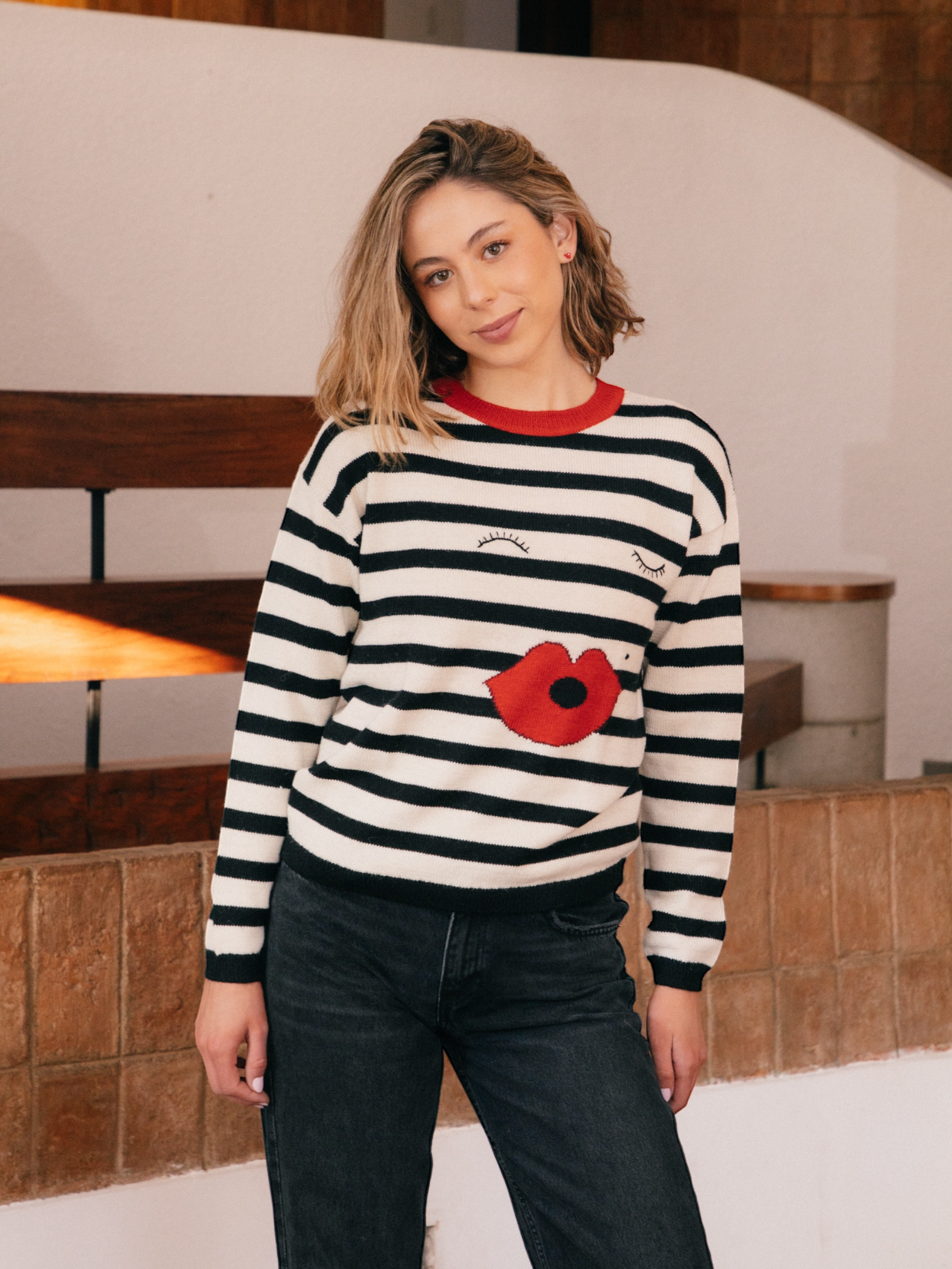 Person wearing a black and white striped sweater with a red poppy design indoors.