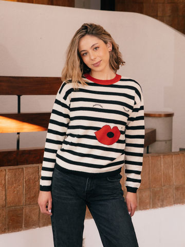 Person wearing a black and white striped sweater with a red poppy design indoors.