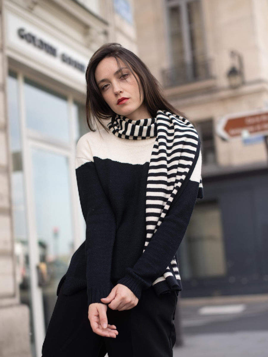Black-and-white striped alpaca scarf featuring an embroidered face motif with closed eyes and red lips styled with a yapa sweater, shown on a model against an outdoor background.
