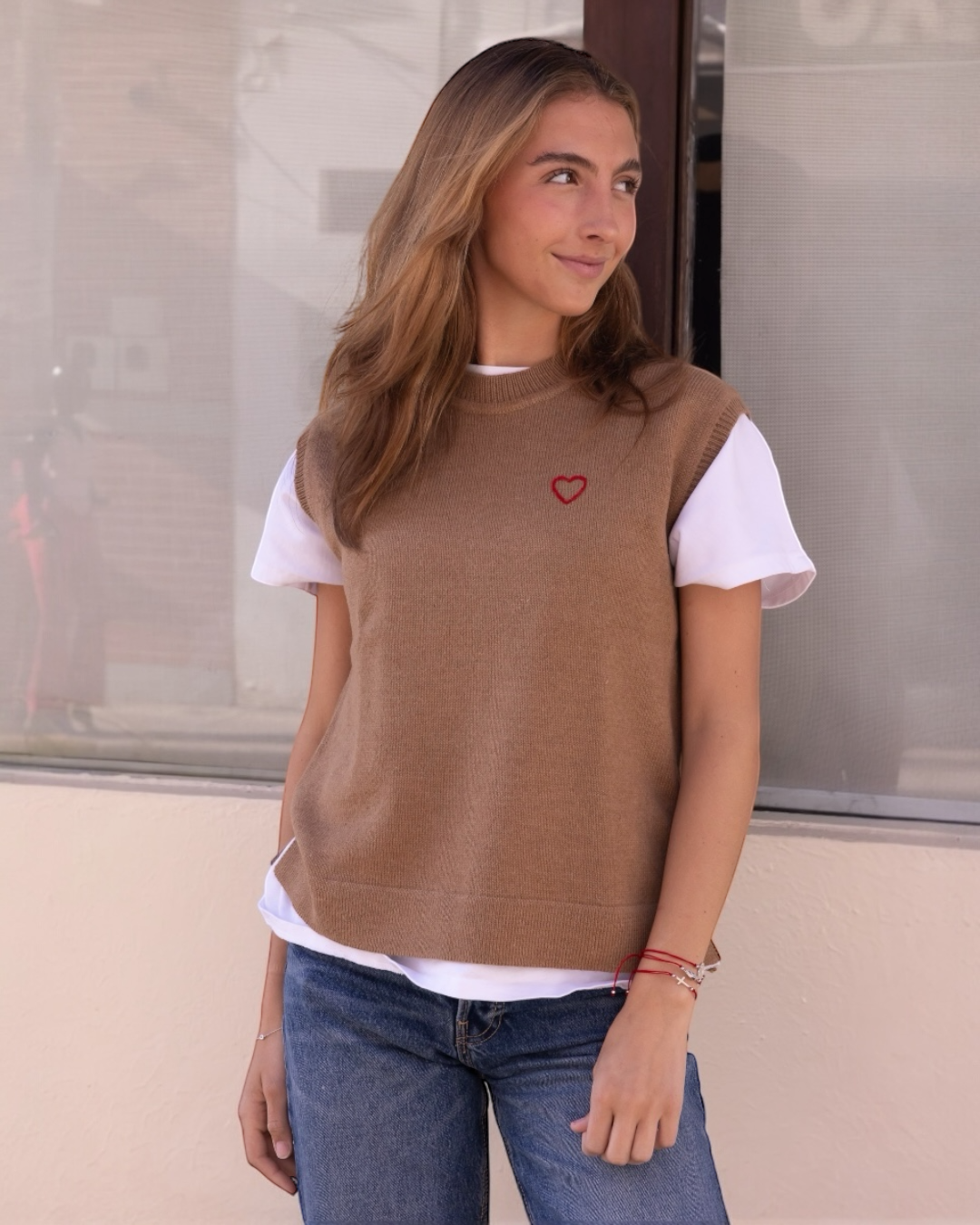 A woman wearing  a knitted alpaca vest with a round neckline, featuring a hand-embroidered heart on the chest.