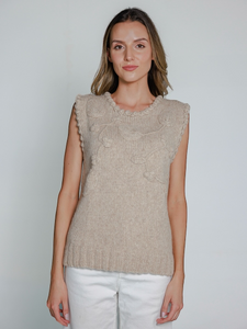 Woman wearing a beige knitted sleeveless top against a plain background