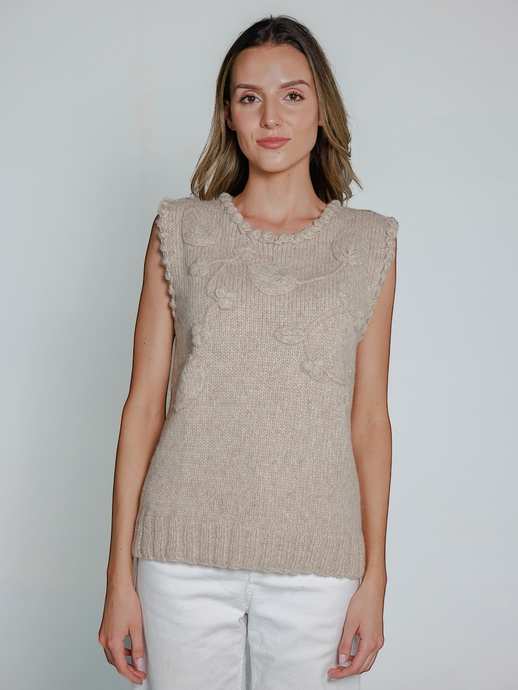 Woman wearing a beige knitted sleeveless top against a plain background