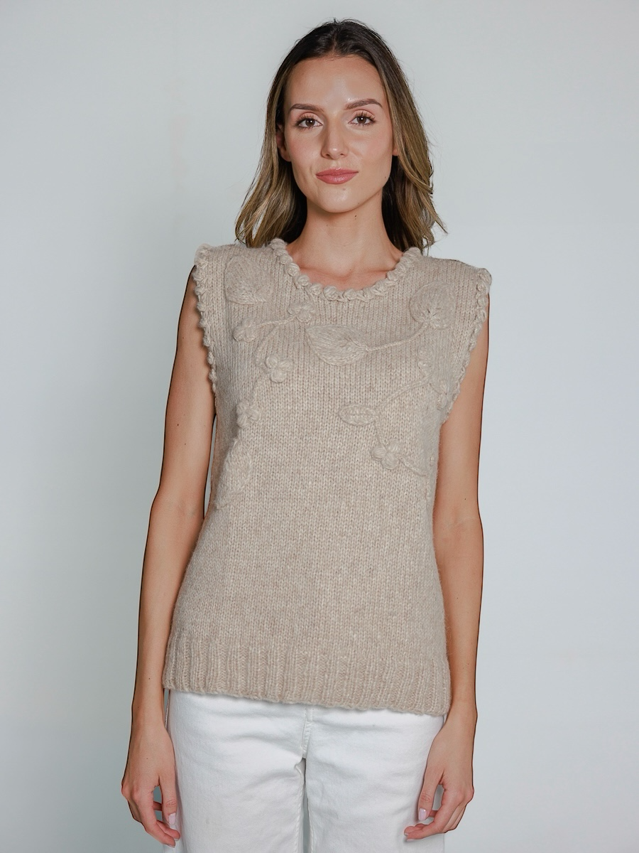 Woman wearing a beige knitted sleeveless top against a plain background