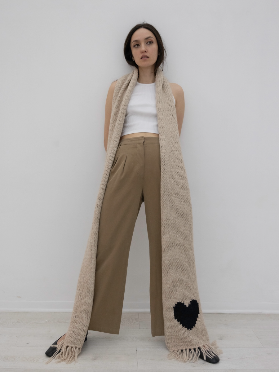 Beige llama scarf featuring a black heart motif on one end with fringed edges, shown against a plain background.