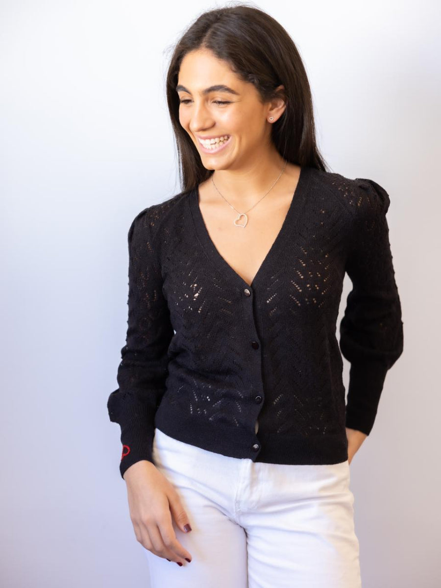 Black alpaca cardigan featuring a delicate open-knit pattern and a small red embroidered heart on the cuff, shown here on a model against a plain background.