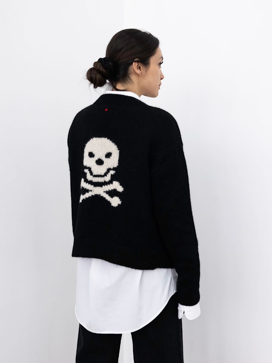 Person wearing a black sweater with a skull design on the back against a white background