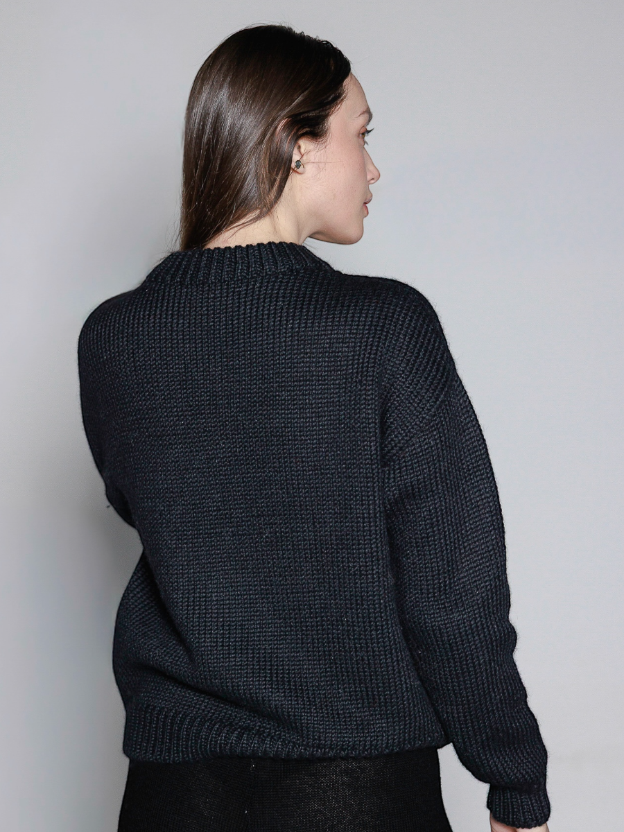 model wearing a black sweater with a red heart design against a plain background
