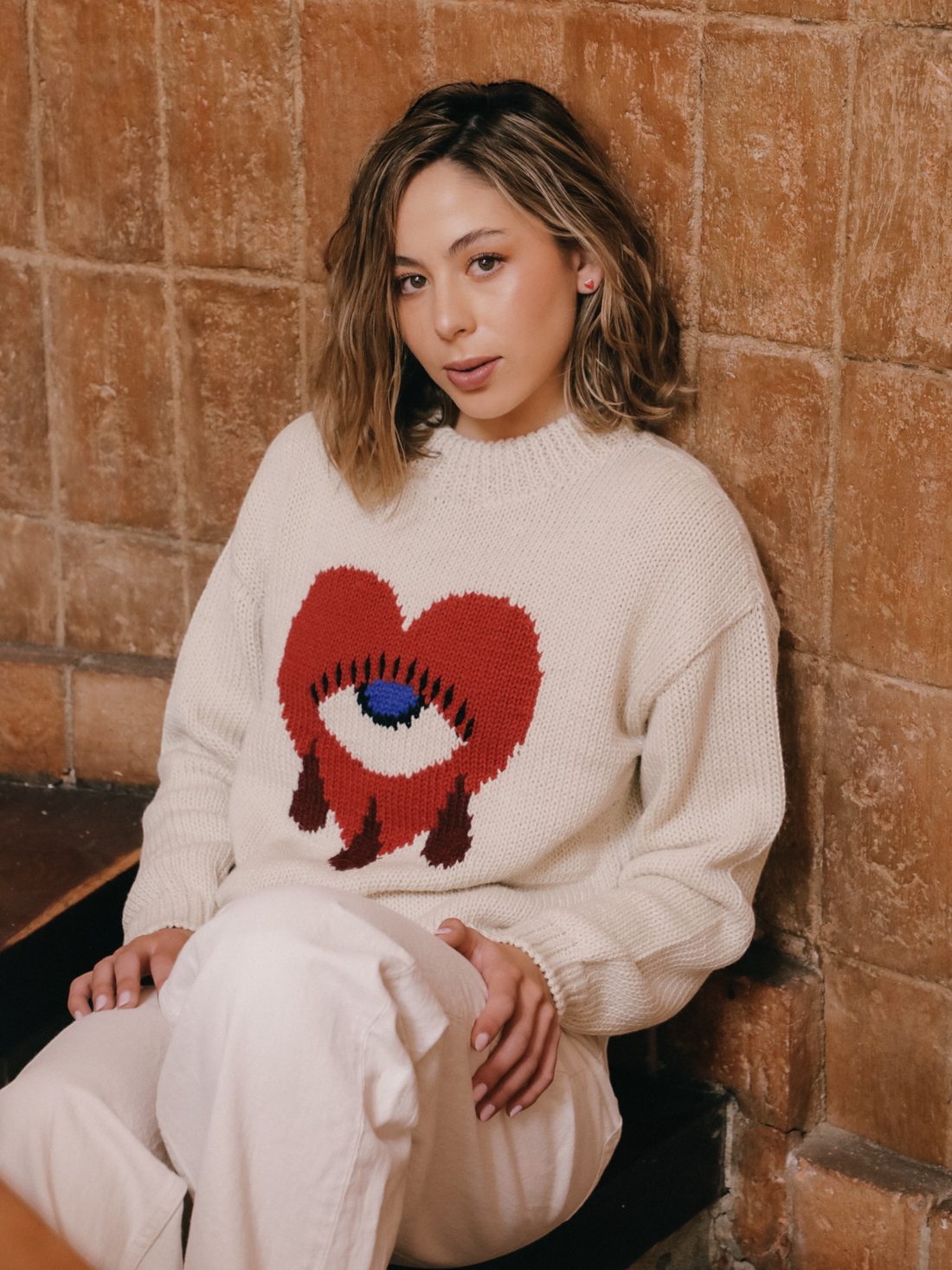 Woman wearing a sweater with a red heart design against a wooden wall.