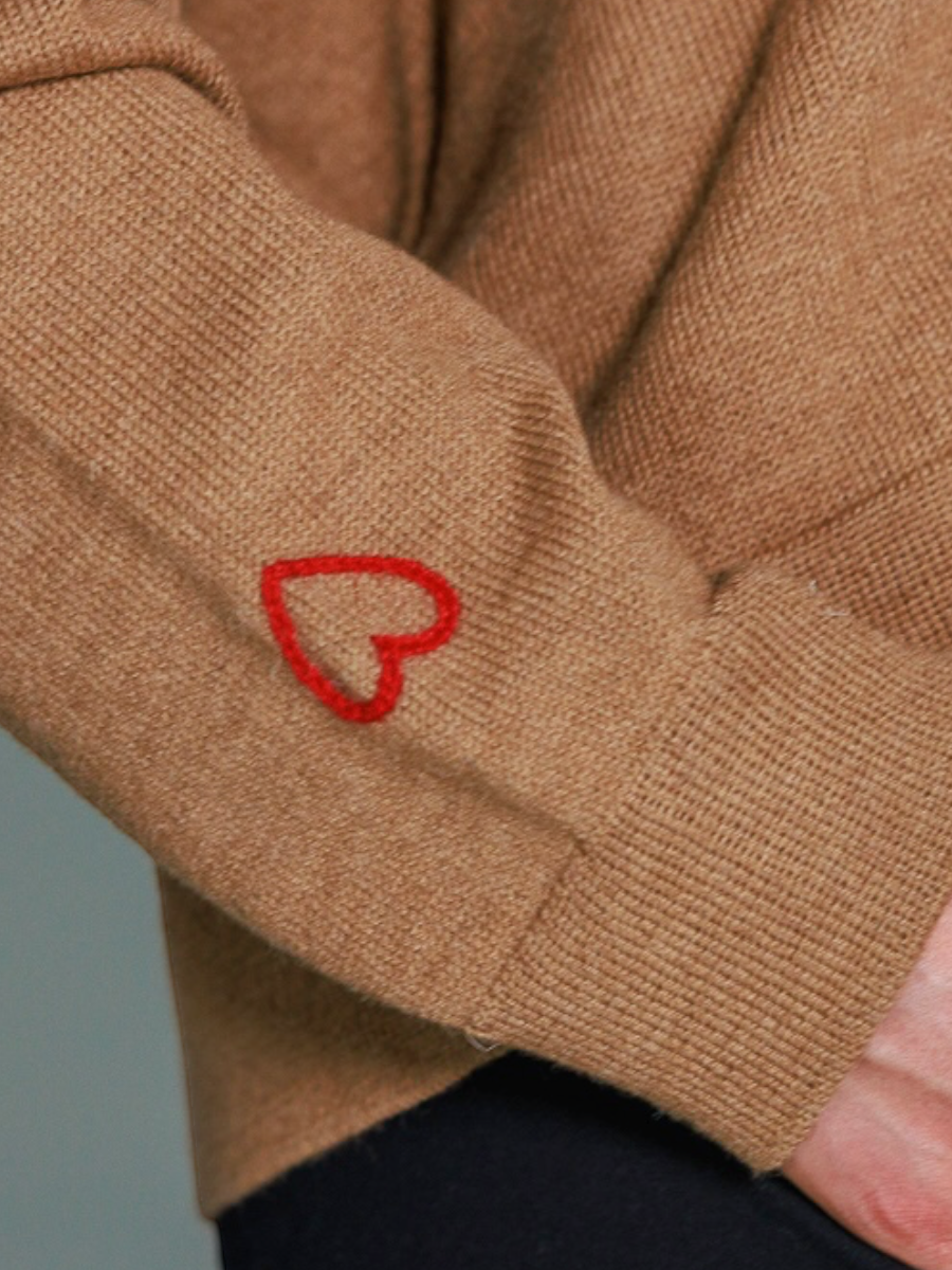 A woman wearing a beige V-neck alpaca wool sweater with long sleeves, paired with blue jeans.