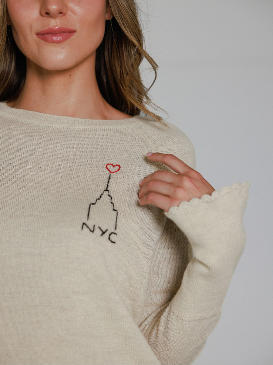 Off white sweater with embroidered design of the Empire State Building and 'NYC' on a white background